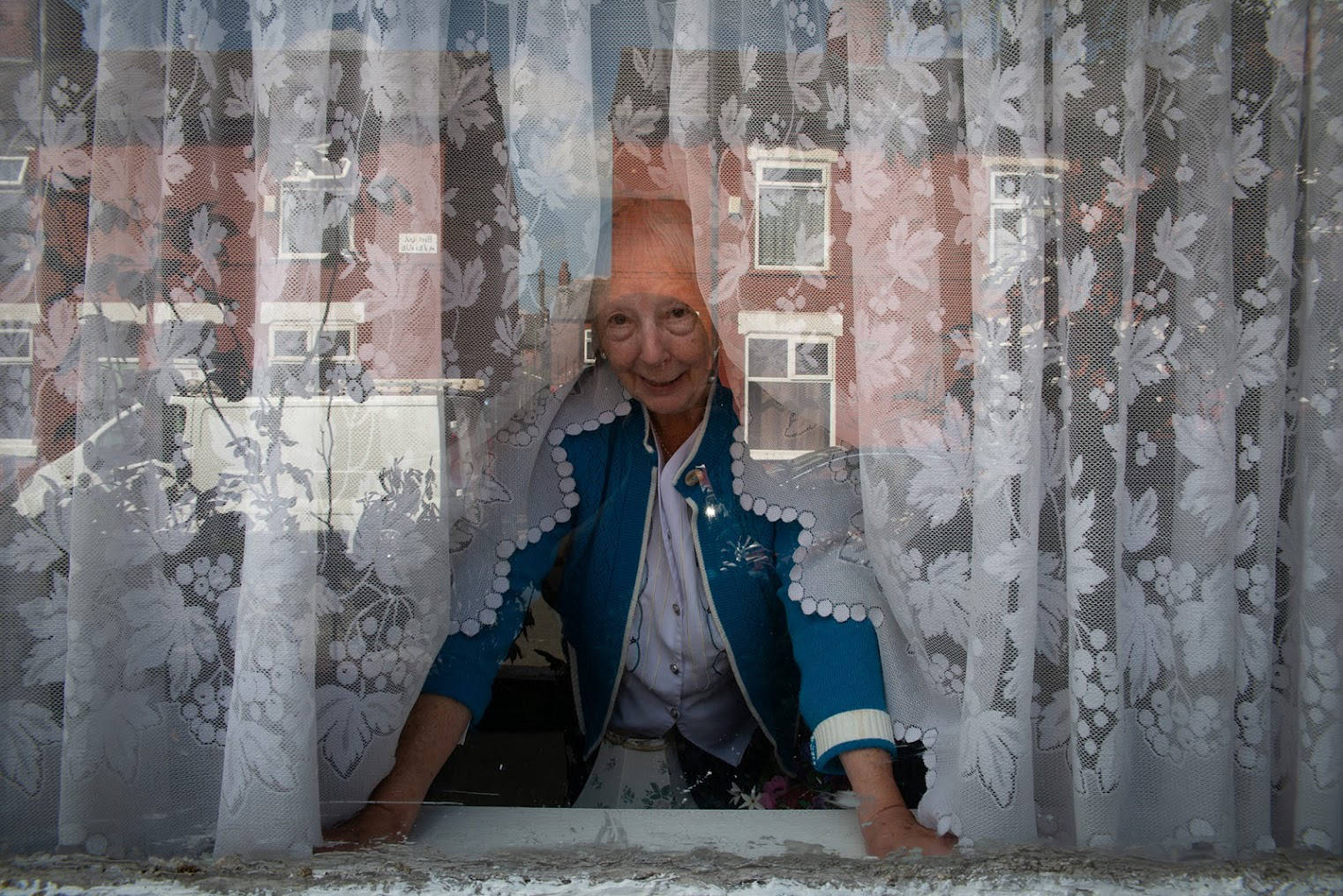 An elderly woman looking outside her window.
