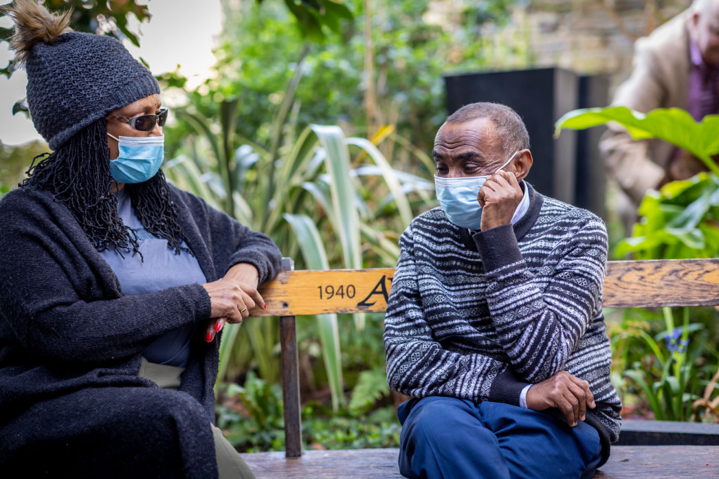 Two people sitting on a bench with face masks on 