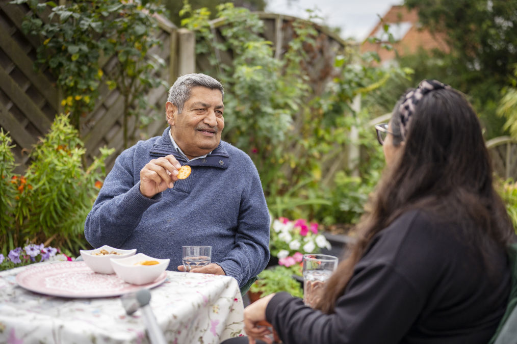 A South Asian man eating and laughing in a garden